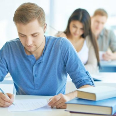 Portrait of handsome student carrying out test at lesson with groupmates on background